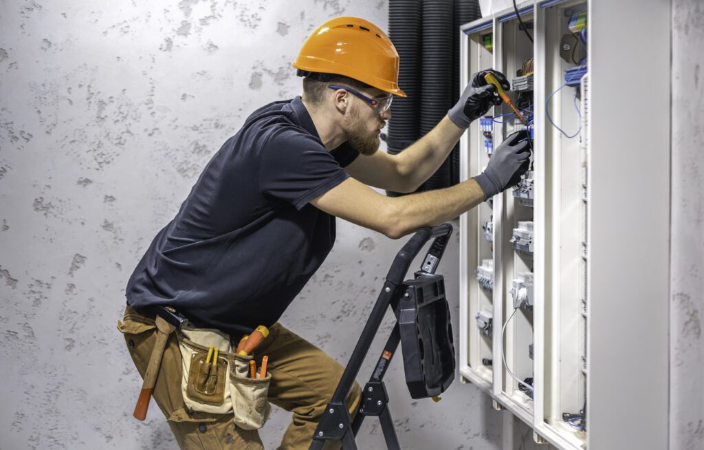 A male electrician works in a switchboard with an electrical connecting cable.